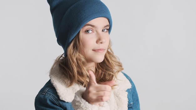 Free photo portrait of pretty blond teenage girl pointing index fingers on camera looking cool over white background