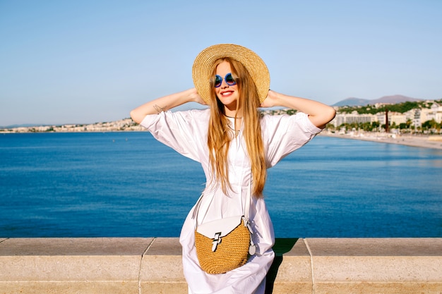 Ritratto di donna turistica abbastanza bionda in posa in costa azzurra, indossando abiti estivi alla moda
