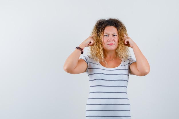 Foto gratuita ritratto di una bella donna bionda che tiene le dita sulle tempie con una maglietta a righe e sembra una vista frontale dispiaciuta