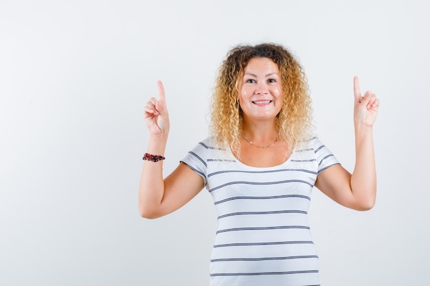 Portrait of pretty blonde woman pointing up in striped t-shirt and looking joyful front view