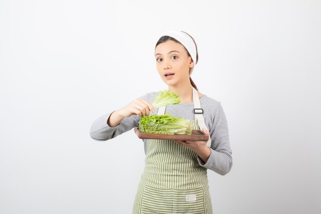 Portrait of a pretty cute woman holding a wooden board with fresh lettuce 