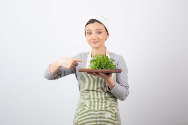Portrait of a pretty cute woman pointing at a wooden board with fresh parsley