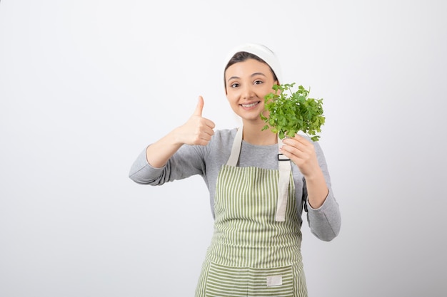 Portrait of a pretty cute woman with beam of fresh parsley showing a thumb up 