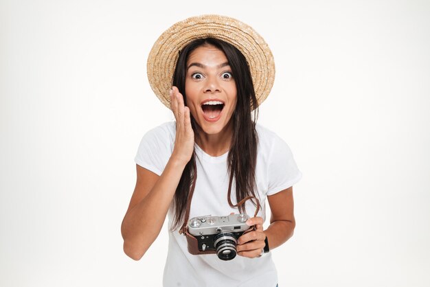 Portrait of pretty excited woman in hat holding a camera