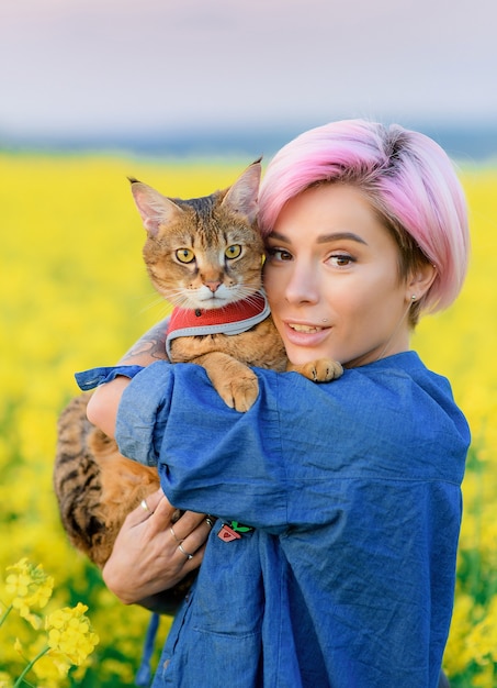 Download Free Stock Photo: Portrait of pretty female with pink hair, resting on nature, holding cat on her arms and looking at camera