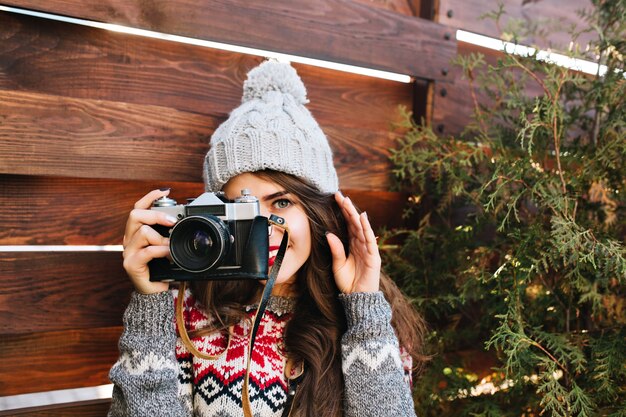Портрет красивой девушки в вязаной шапке, весело делая фото на камеру на деревянном.