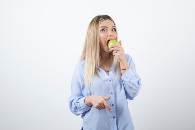 녹색 신선한 사과를 먹고 서 있는 예쁜 여자 모델의 초상화.