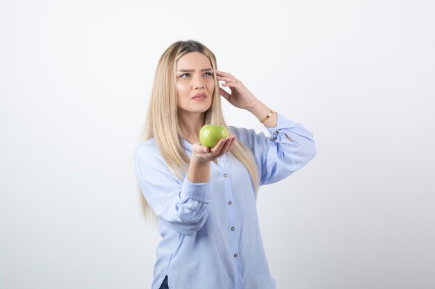 портрет красивой девушки модели стоя и держа зеленое свежее яблоко.