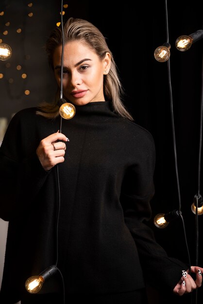 Portrait of pretty girl posing in dark sweater standing near lamps .