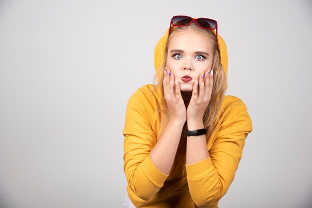 Portrait of pretty girl in yellow hoodie posing with glasses.