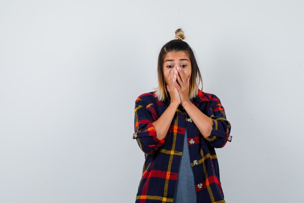 Portrait of pretty lady holding hands on face in casual shirt and looking astonished front view