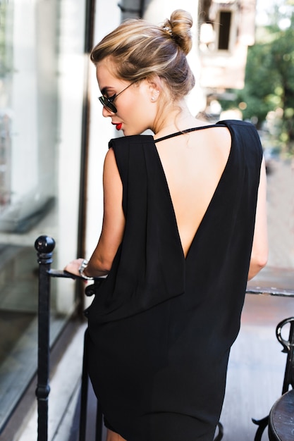 Free photo portrait  pretty model in black dress with naked back on terrace. she is looking down.