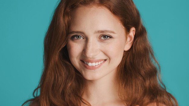 Portrait of pretty smiling redhead girl joyfully looking in camera over colorful background