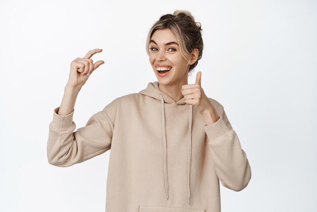 Portrait of pretty smiling woman pinching fingers and showing thumbs up recommending small size thing little tiny object against copy space white background