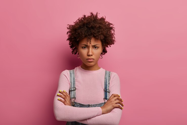 Free Photo portrait of pretty sulking young woman stands dissatisfied, keeps hands crossed, being insulted by someone and waits for apologize, looks from under forehead, poses angry against pink wall