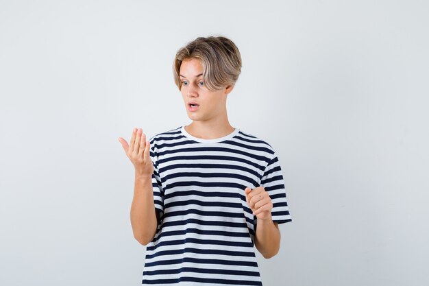 Portrait of pretty teen boy looking at his palm in striped t-shirt and looking shocked front view