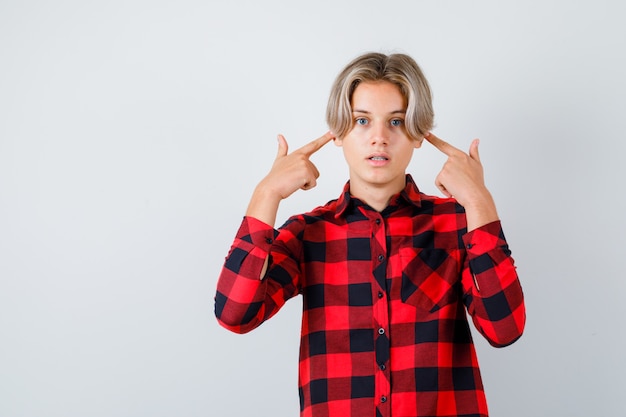 Portrait of pretty teen boy plugging ears with fingers in checked shirt and looking scared front view