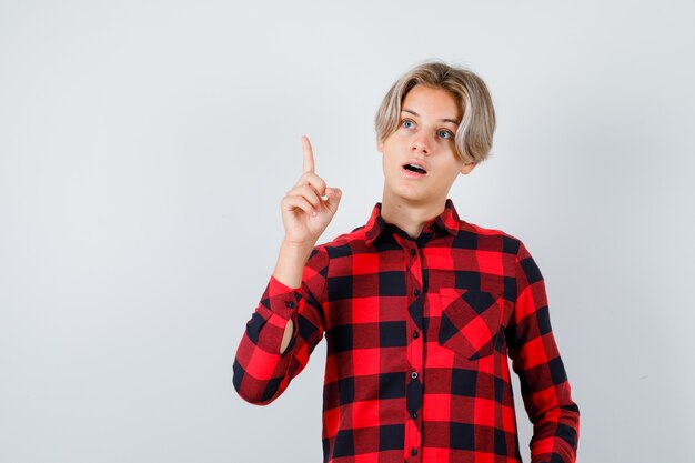 Portrait of pretty teen boy pointing up, looking away in checked shirt and looking smart front view
