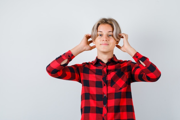 Foto gratuita ritratto di un bel ragazzo adolescente con le mani vicino alle orecchie in camicia a quadri e con una vista frontale allegra