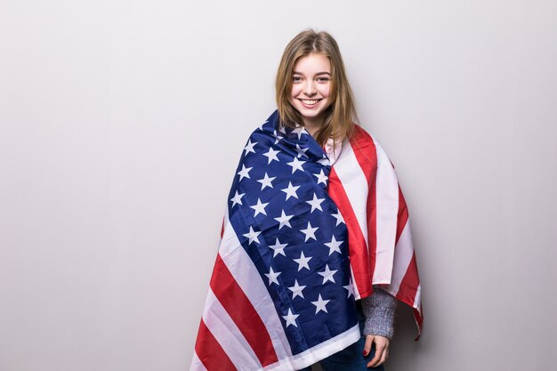 Portrait of pretty teen girl holding USA flag isolated on gray. 4th July celebration.