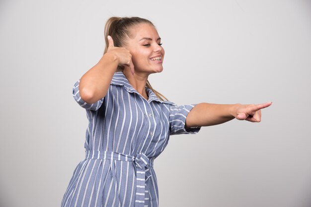 灰色の壁に誰かを呼ぶきれいな女性のポートレート。