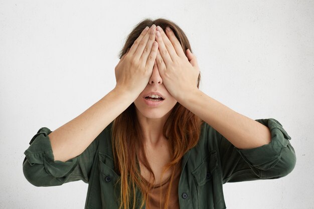 portrait of pretty woman covering her eyes with hands. Young desperate woman hiding her face not wanting to see anybody.