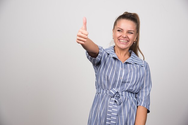 Portrait of pretty woman giving thumbs up on gray wall.