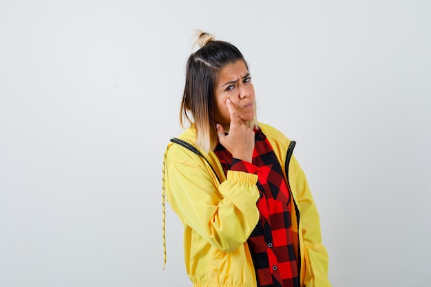 Portrait of pretty woman pointing at her eyelid in shirt, jacket and looking sad front view