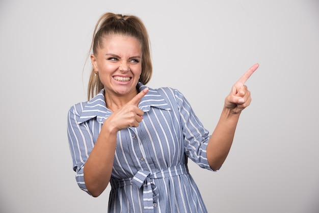 Portrait of pretty woman pointing at something on gray wall.