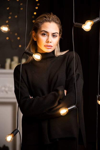 램프 근처에 서 있는 어두운 스웨터에 포즈를 취하는 예쁜 여자의 초상화.