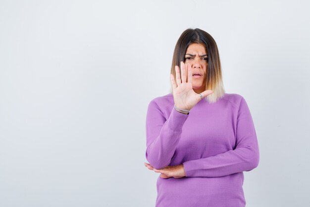 Портрет красивой женщины, показывающей жест стоп в фиолетовом свитере и серьезной вид спереди