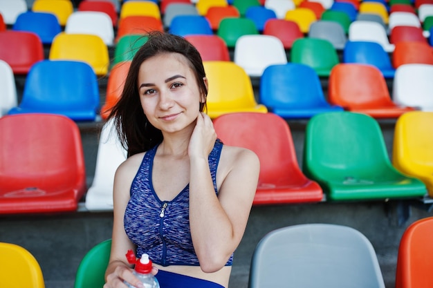 Portrait of a pretty woman in sportswear sitting and drinking water in the stadium
