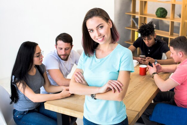 Portrait of a pretty woman with arm crossed standing with her friends sitting behind