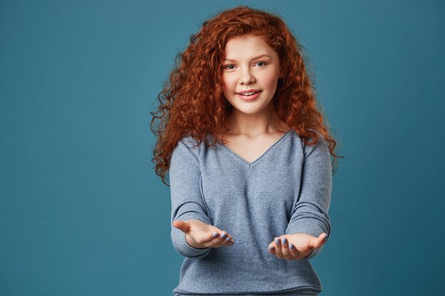 Portrait of pretty woman with wavy red hair and freckles in grey shirt with happy and relaxed expression.