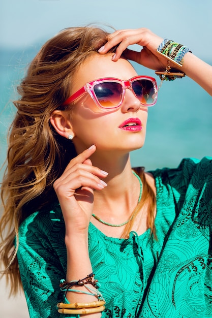 Portrait of pretty young blonde beautiful woman in cool sunglasses posing on the sunny tropical beach