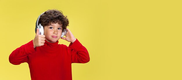 Portrait of pretty young curly boy in red wear on yellow studio background. Childhood, expression, education, fun concept.