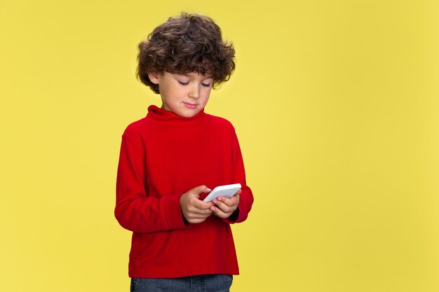 Портрет довольно молодого кудрявого мальчика в красной одежде на желтом фоне студии. Детство, выражение, образование, концепция развлечения.