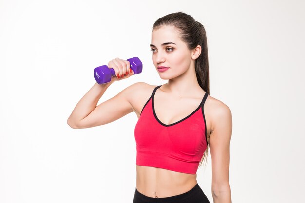 Portrait of a pretty young sportswoman doing exercises with dumbbells isolated on a white wall
