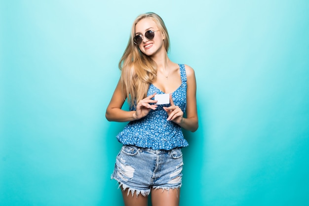 Портрет красивой молодой женщины, одетой в свитер, указывая пальцем на кредитную карту, изолированную на синем фоне