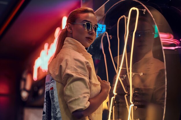 Portrait of pretty young woman in neon lights with darkness around.