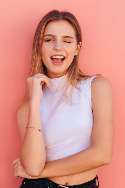 Portrait of a pretty young woman winking against peach backdrop