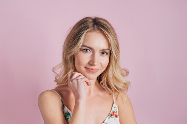 Portrait of pretty young woman with chin on her hand against pink wallpaper