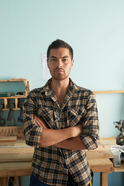 Portrait of professional carpenter standing in the workshop arms folded