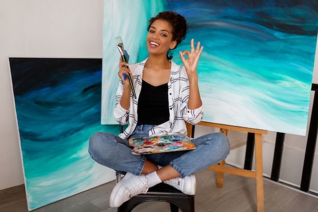 Free photo portrait of professional female artist painting on canvas in studio. woman painter at her  workspace.