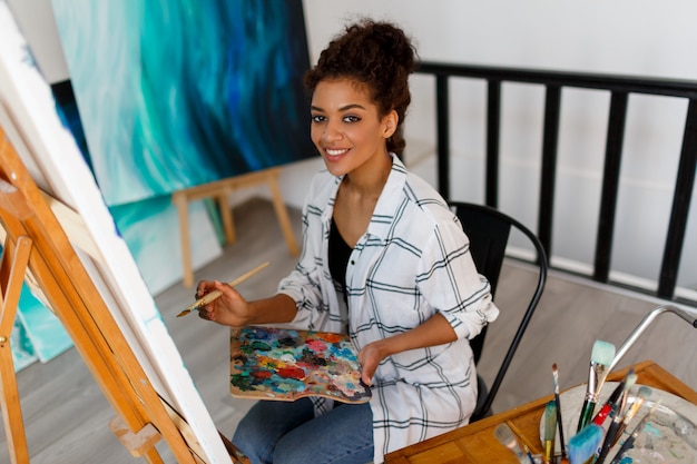 Portrait of professional female artist painting on canvas in studio. Woman painter at her  workspace.