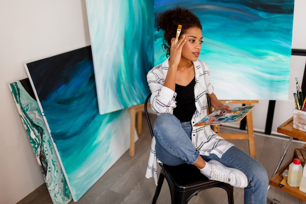 Portrait of professional female artist painting on canvas in studio. Woman painter at her  workspace.