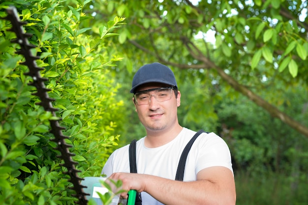 Portrait of professional gardener holding trimmer working in the yard