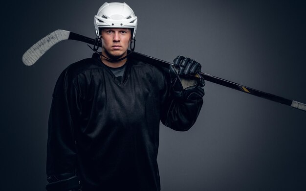 Portrait of professional hockey player holds gaming stick isolated on grey background.