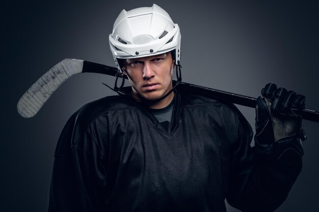 Portrait of professional hockey player holds gaming stick isolated on grey background.