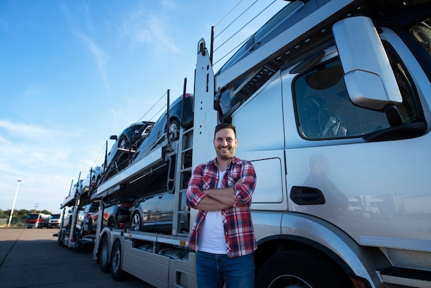 Portrait of professional smiling truck driver with crossed arms transporting cars to the market